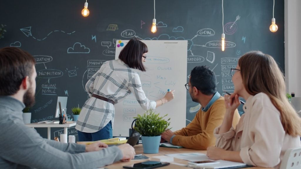 Creative multi-ethnic team are talking sharing ideas while young woman is writing on whiteboard in creative office. People and brainstorming in workplace.